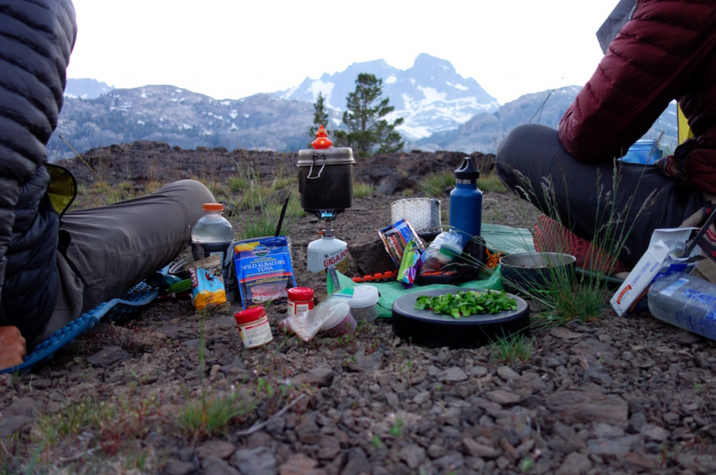Two individuals enjoying wild cooking amidst stunning mountain scenery, using fresh ingredients.